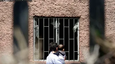 El Desconcierto | 30012 una persona con su hijo en brazos viendo una ventana rota.webp