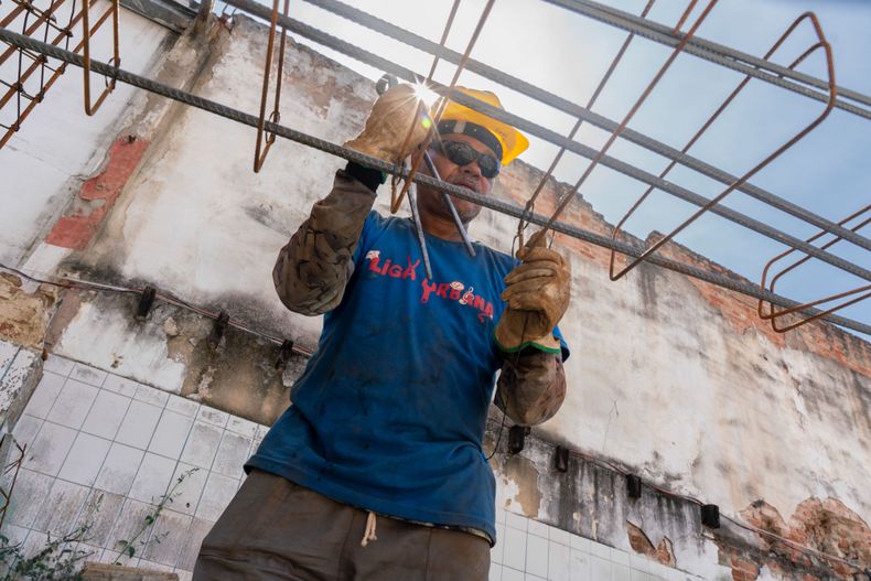 Integrante de la cooperativa Liga Urbana, vinculada al Movimiento Nacional de Lucha por la Vivienda (MNLM), en obra colectiva en la Región Portuaria de Río. Frente a un mercado inmobiliario concentrado y al crecimiento de lanzamientos privados, movimientos sociales impulsan modelos cooperativos y autogestionados como alternativa de acceso a la vivienda digna. En un país donde millones viven en condiciones inadecuadas o en alquiler con sobrecarga de renta, la organización comunitaria se convierte en herramienta de resistencia urbana. Región Portuária, Río de Janeiro, Brasil.